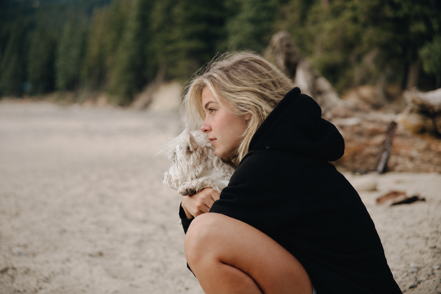 Lily holding a small white dog on a beach